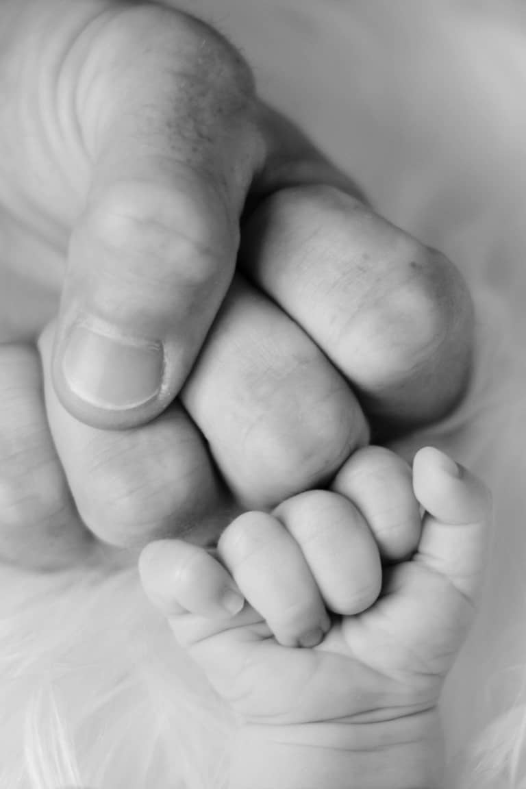 Die Hand eines Neugeborenen berührt die Hand seines Vaters