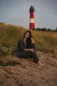 Nicole Heinze sitzt am Strand mit Leuchtturm im Hintergrund